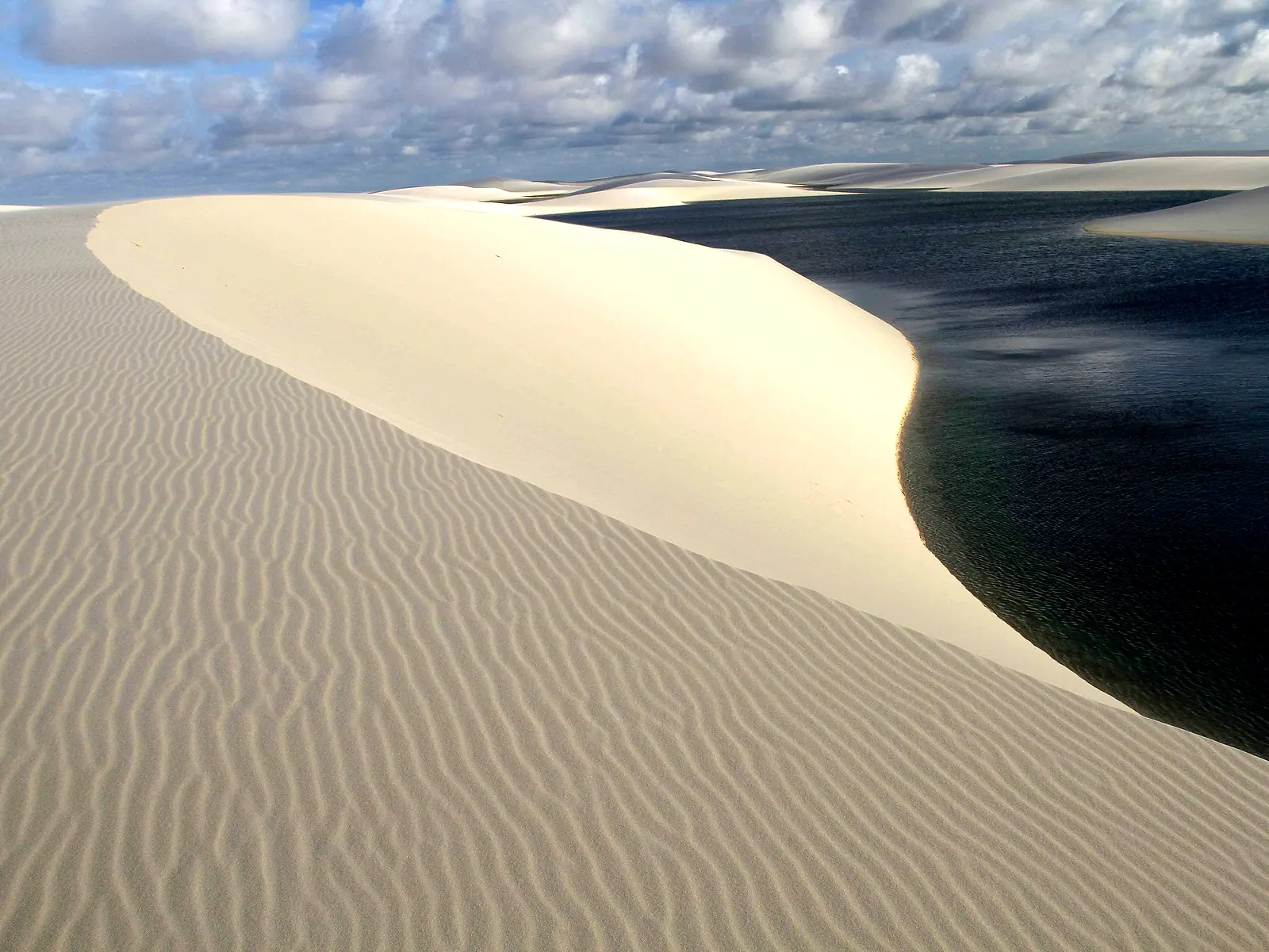 Crista de duna com ondulações na areia ao lado da Lagoa das Andorinhas, de água azul-escura