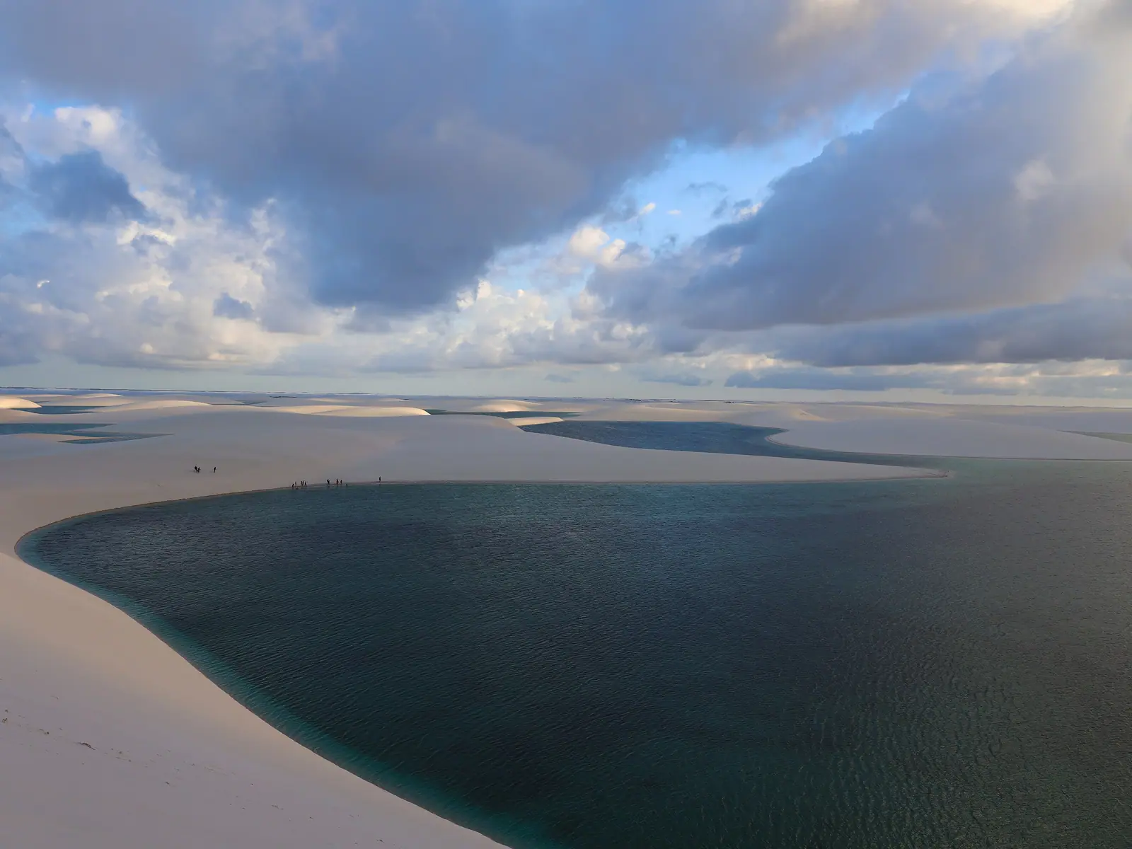 Lagoa azul-escura entre dunas brancas sob céu de nuvens
