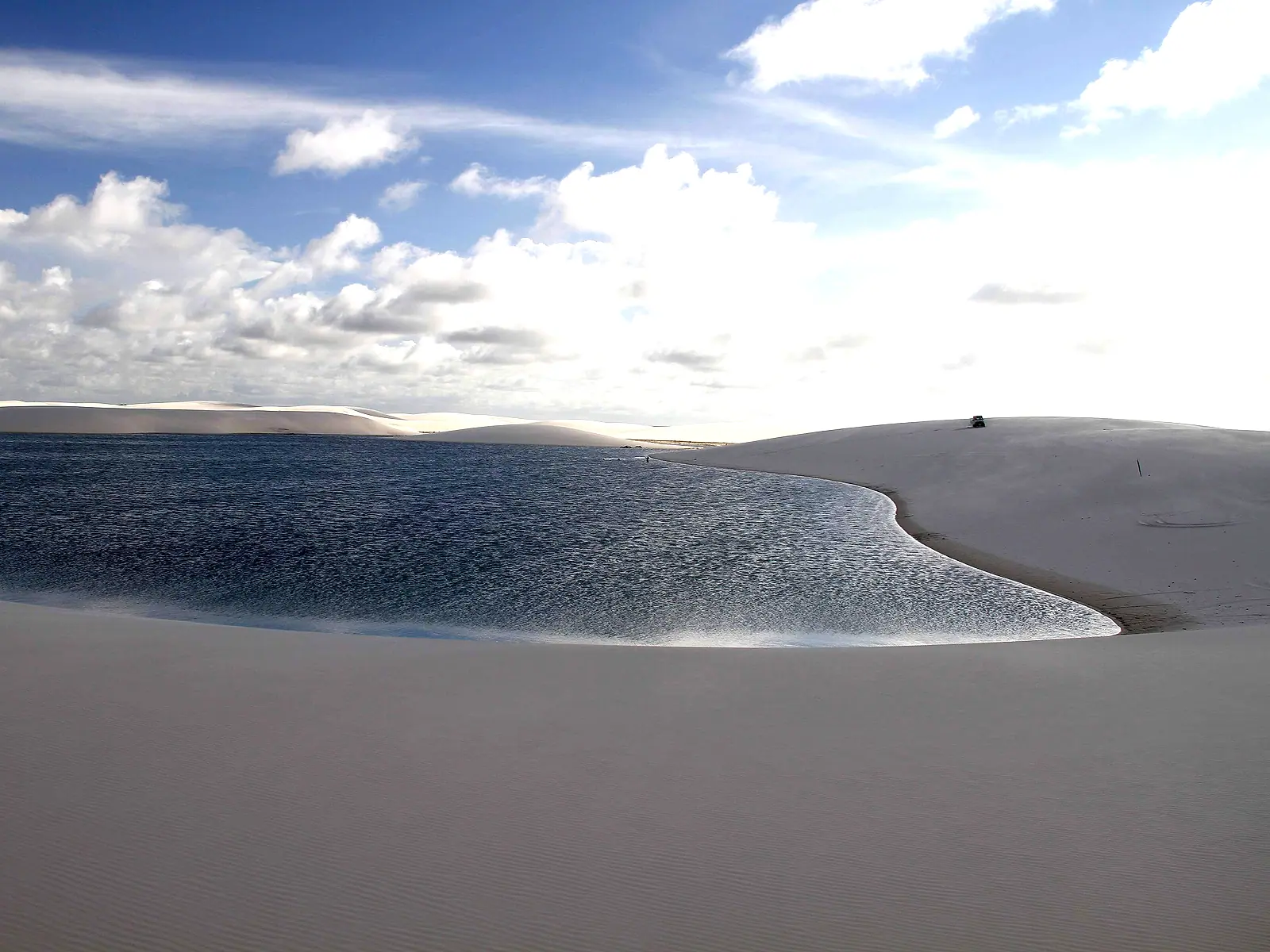 Lagoa ampla entre dunas brancas, com céu azul e nuvens