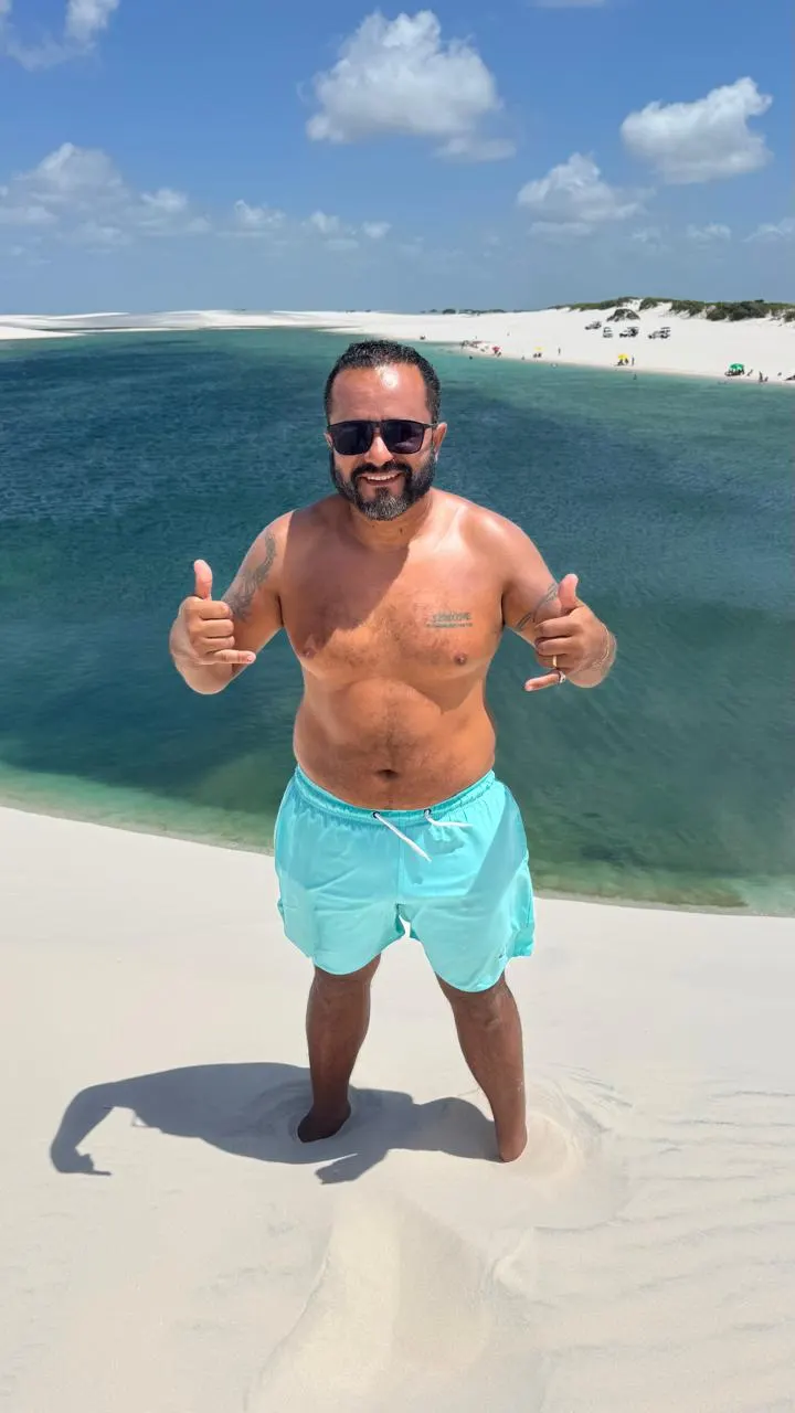 Visitante sorrindo no alto da duna, com a lagoa azul-esverdeada atrás