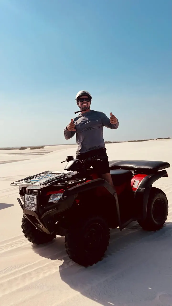 Visitante de capacete sobre um quadriciclo nas dunas, fazendo sinal de positivo