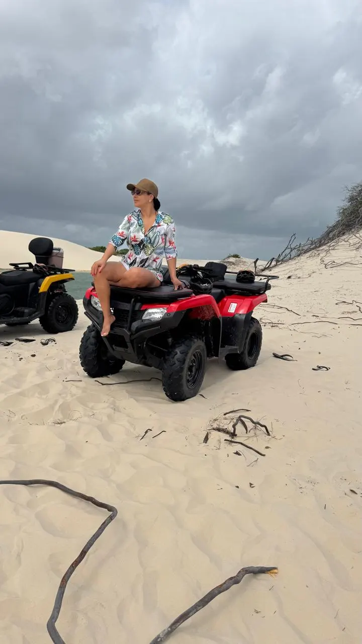 Visitante sentada em um quadriciclo vermelho na areia, com a lagoa ao fundo
