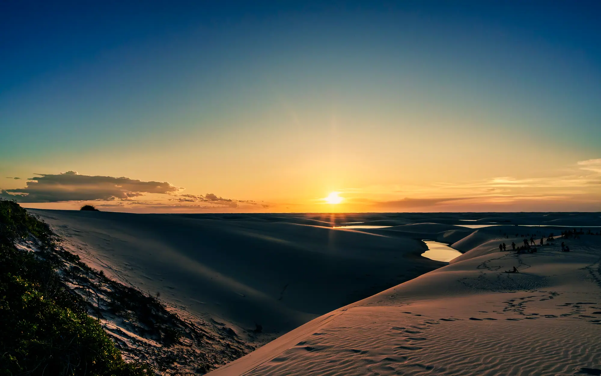 Pôr do sol visto do alto de uma duna, com lagoas e o horizonte dourado